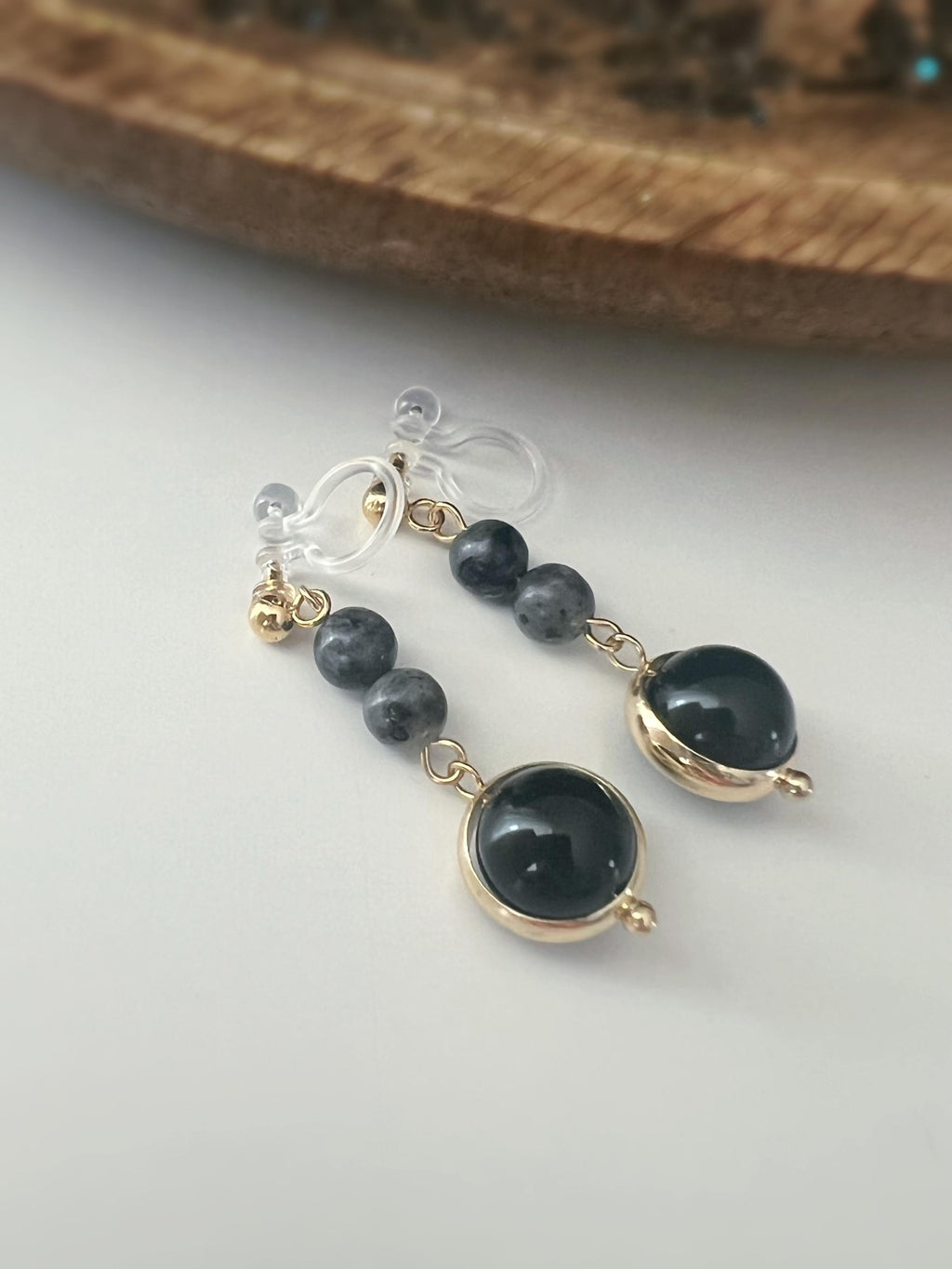 Boucles d'oreilles CLIPS pendantes couleur or, ornées de perles noires et de pierres naturelles grises. Parfaites pour un style raffiné.