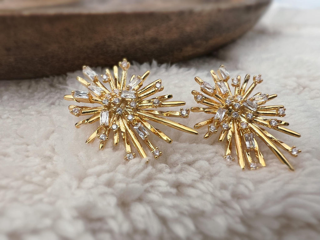 Clips d'oreilles dorés en forme de rayons lumineux, sertis de cristaux étincelants. Une touche glamour idéale pour sublimer vos tenues.
