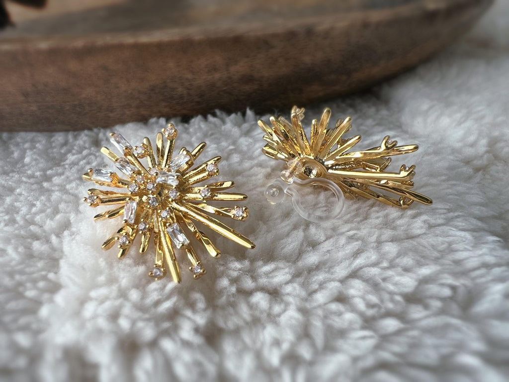 Clips d'oreilles dorés en forme de rayons lumineux, sertis de cristaux étincelants. Une touche glamour idéale pour sublimer vos tenues.