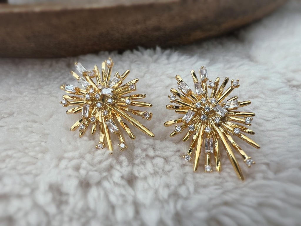 Clips d'oreilles dorés en forme de rayons lumineux, sertis de cristaux étincelants. Une touche glamour idéale pour sublimer vos tenues.