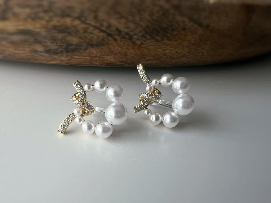 Boucles d’oreilles clip forme de couronne ornées perles blanches, strass scintillants. Finition dorée raffinée pour une touche sophistiquée.