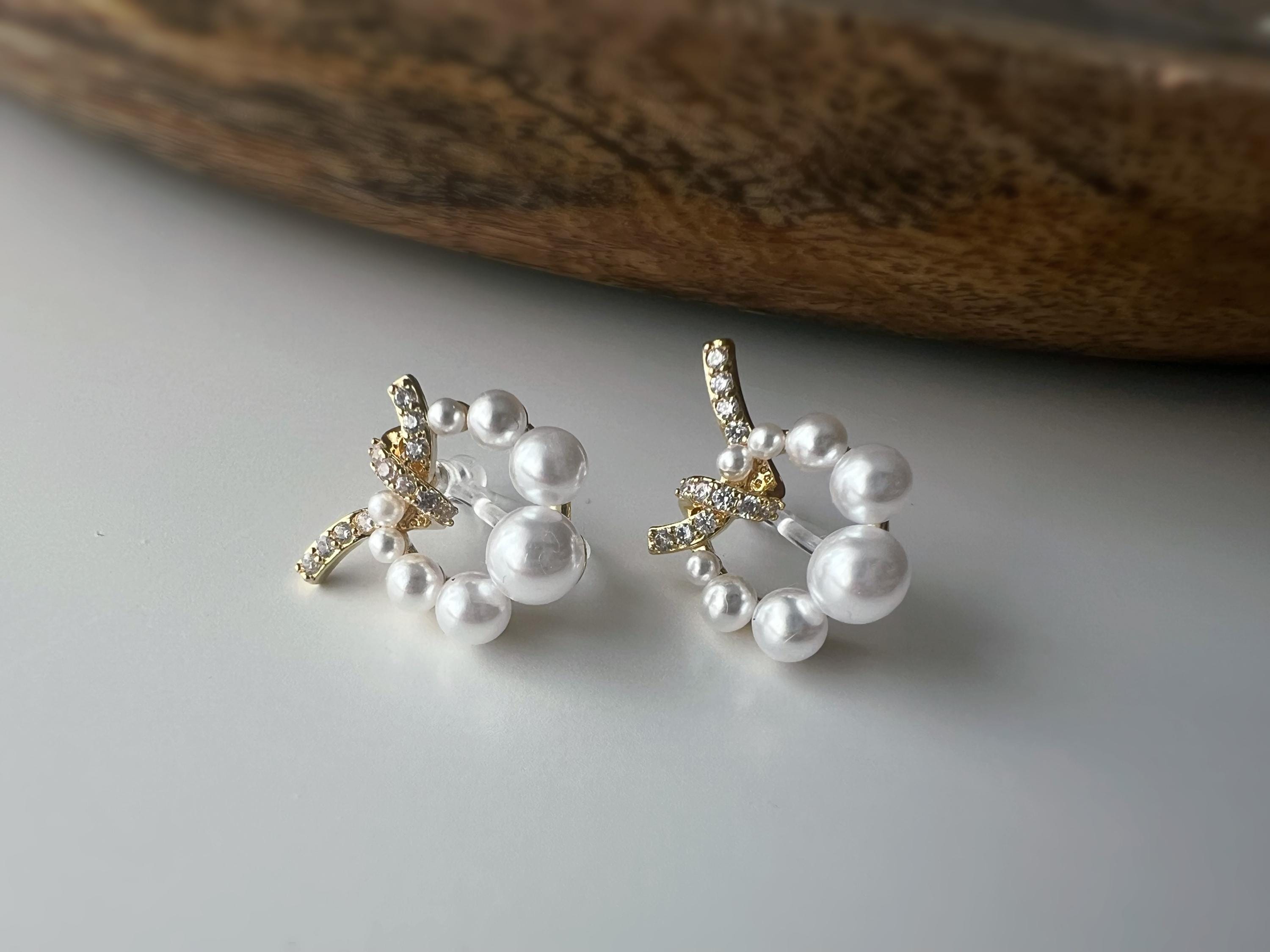 Boucles d’oreilles clip forme de couronne ornées perles blanches, strass scintillants. Finition dorée raffinée pour une touche sophistiquée.