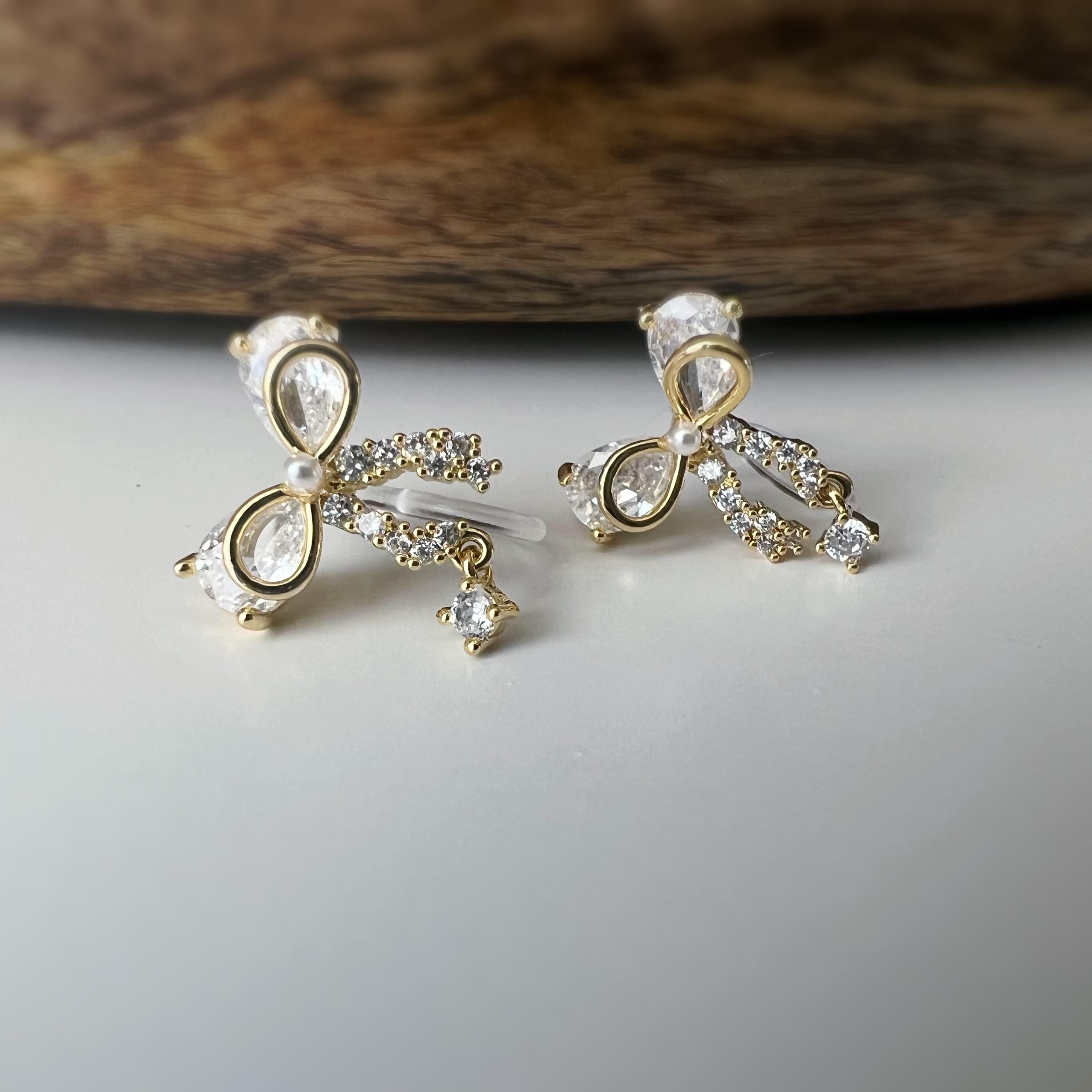 Clips d’oreilles papillon en strass, disponibles en doré et argenté. Design raffiné pour un look délicat, sans perçage.