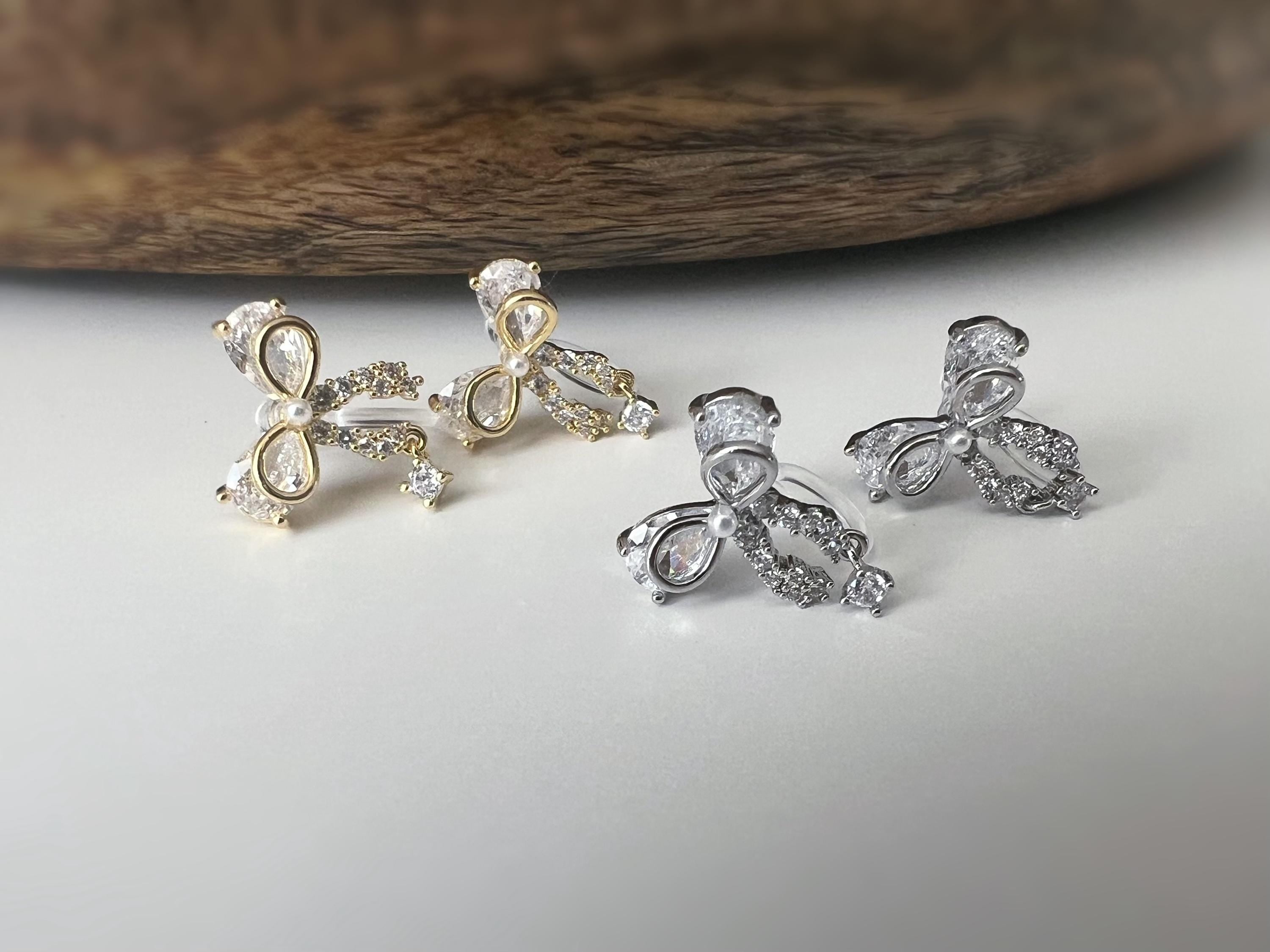 Clips d’oreilles papillon en strass, disponibles en doré et argenté. Design raffiné pour un look délicat, sans perçage.