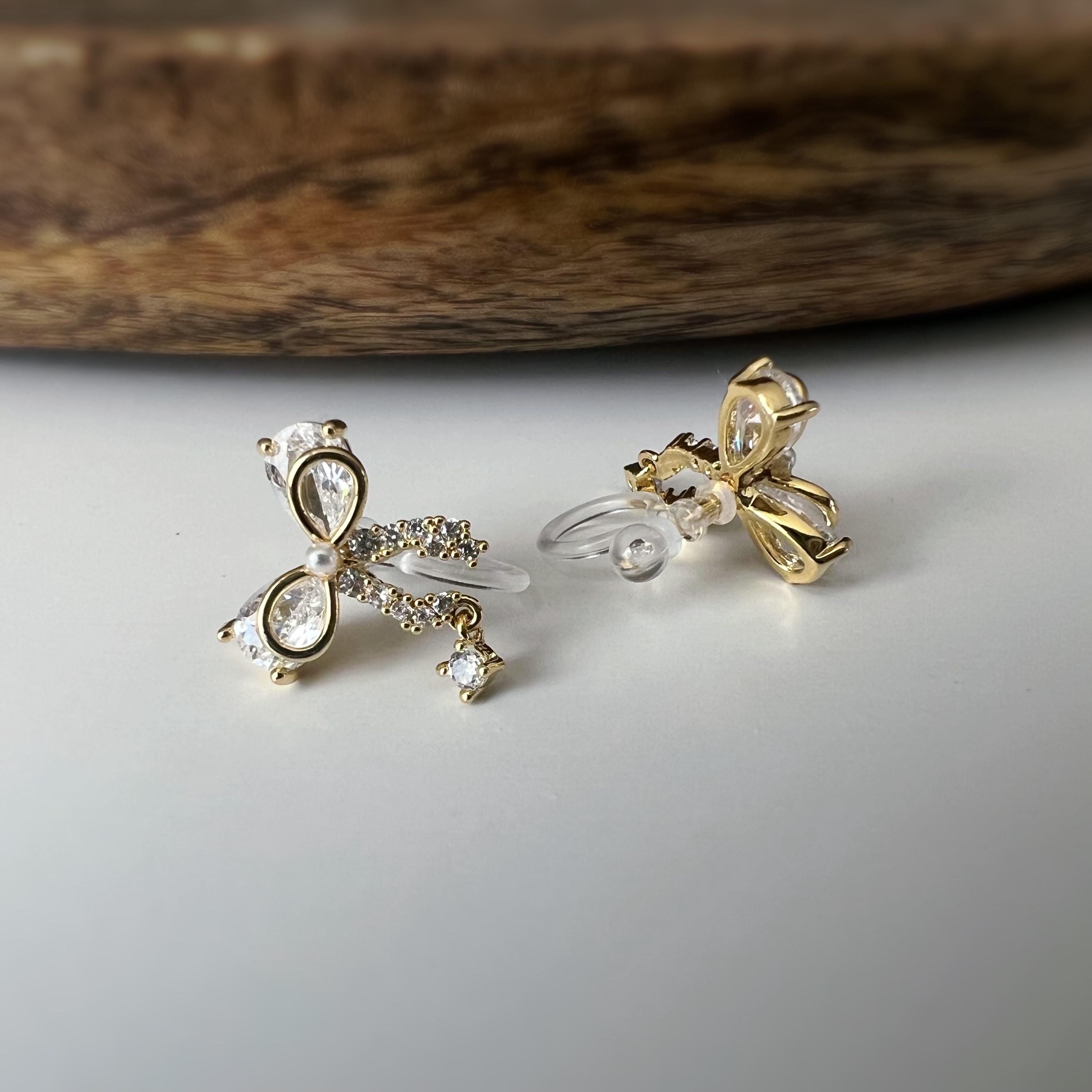 Clips d’oreilles papillon en strass, disponibles en doré et argenté. Design raffiné pour un look délicat, sans perçage.