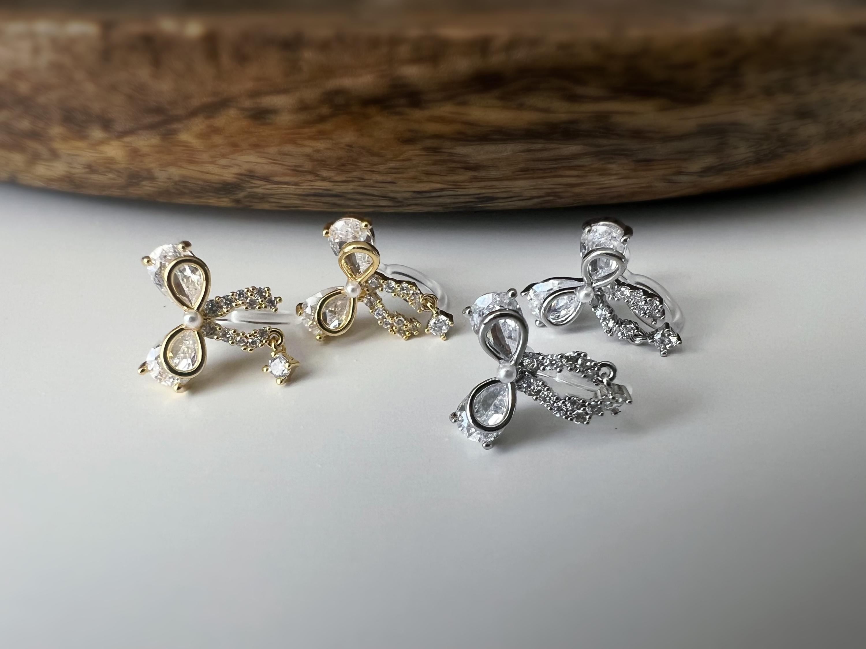 Clips d’oreilles papillon en strass, disponibles en doré et argenté. Design raffiné pour un look délicat, sans perçage.