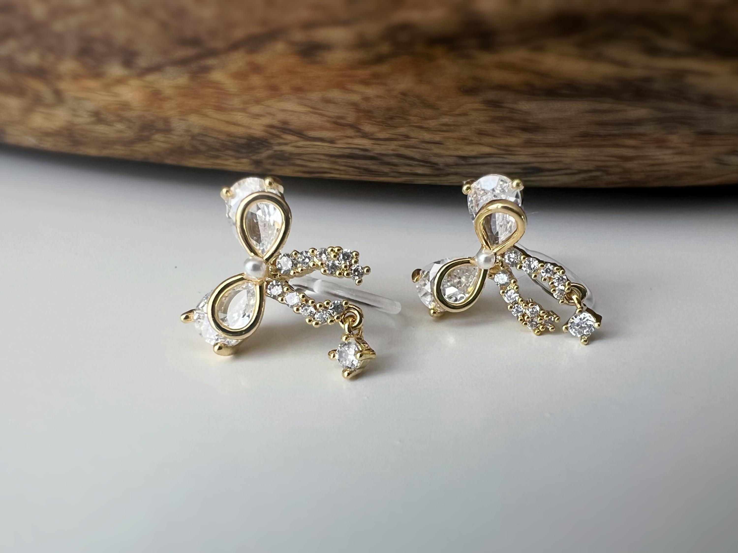 Clips d’oreilles papillon en strass, disponibles en doré et argenté. Design raffiné pour un look délicat, sans perçage.