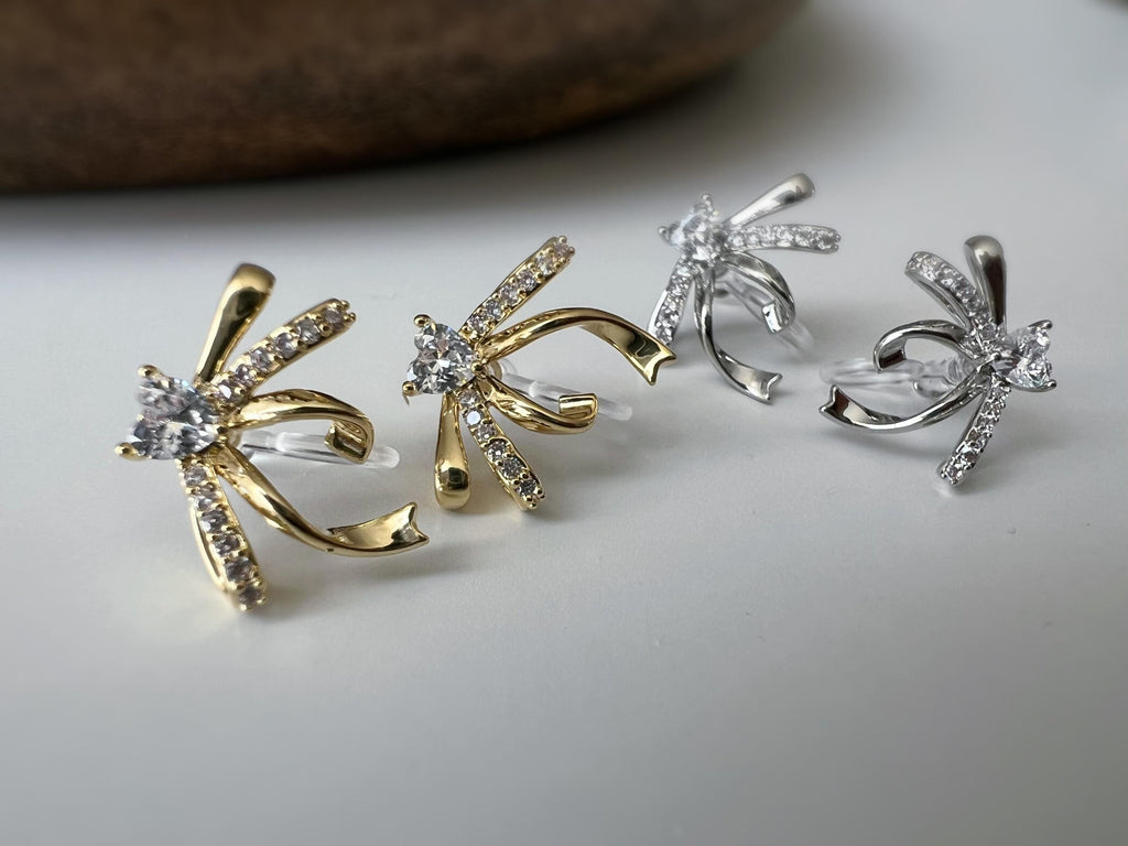 Clips d’oreilles élégants en forme de nœud scintillant Or / Argent sertis de strass étincelants. Bijou raffiné pour un style chic et féminin