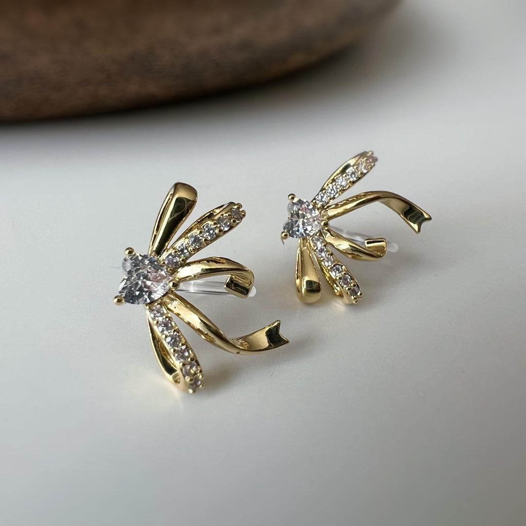 Clips d’oreilles élégants en forme de nœud scintillant Or / Argent sertis de strass étincelants. Bijou raffiné pour un style chic et féminin