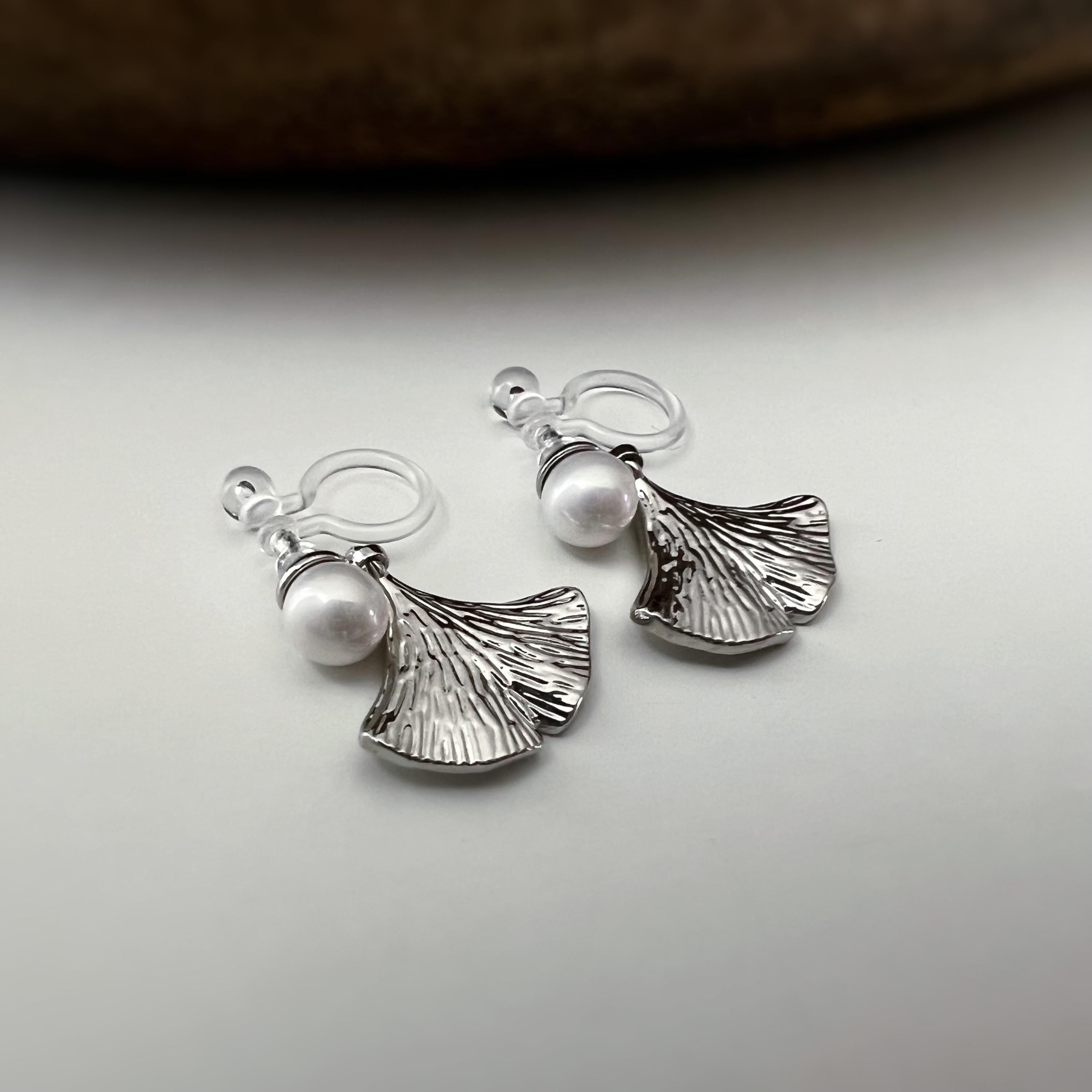 Clips d’oreilles élégants ornés d’une perle blanche et d’un pendentif feuille de ginkgo Or / Argent. Un bijou raffiné, chic et intemporel.