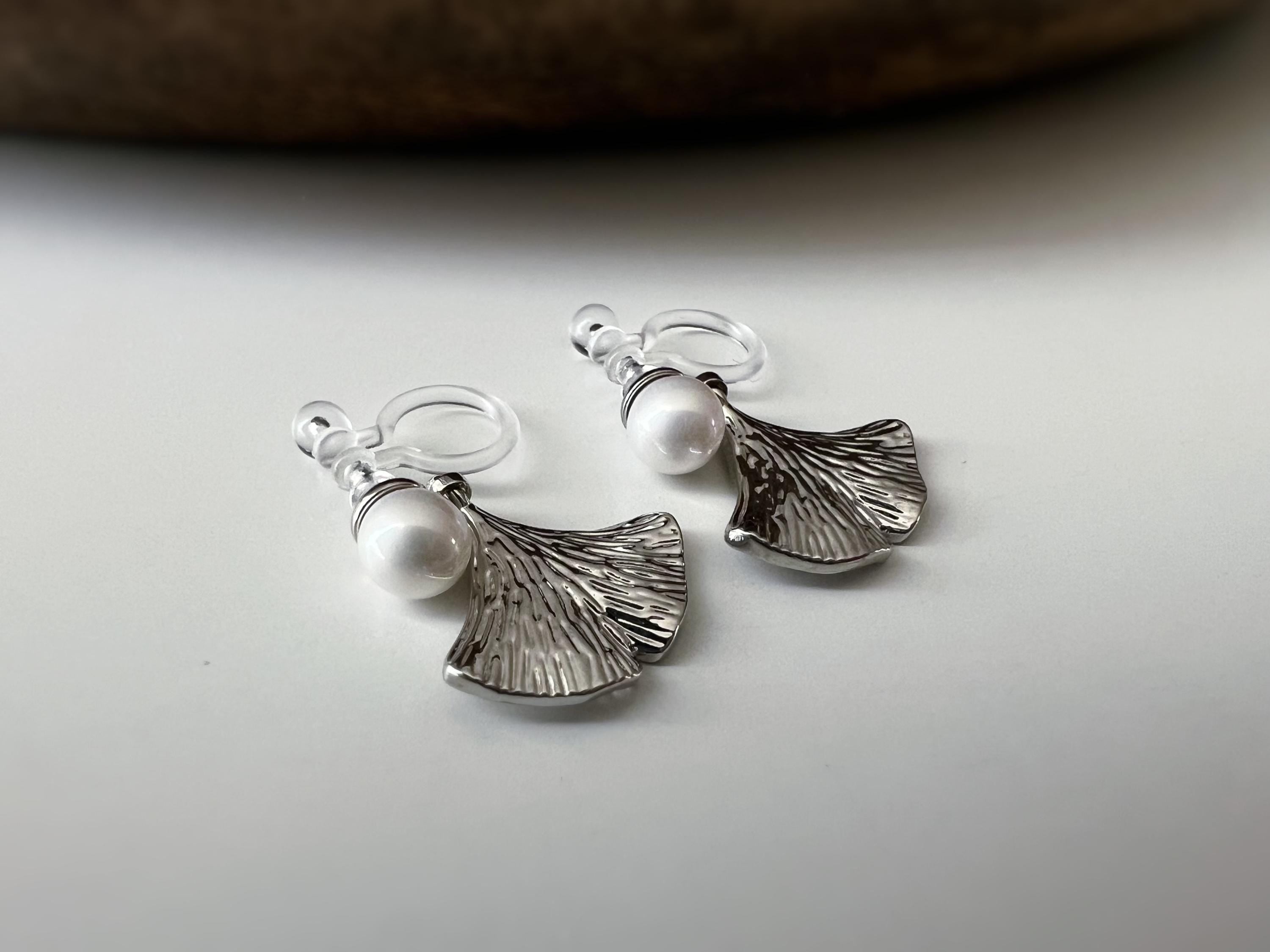 Clips d’oreilles élégants ornés d’une perle blanche et d’un pendentif feuille de ginkgo Or / Argent. Un bijou raffiné, chic et intemporel.