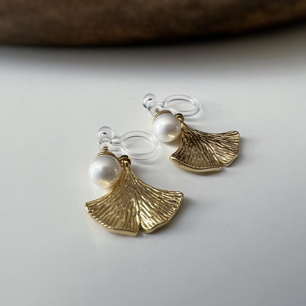 Clips d’oreilles élégants ornés d’une perle blanche et d’un pendentif feuille de ginkgo Or / Argent. Un bijou raffiné, chic et intemporel.