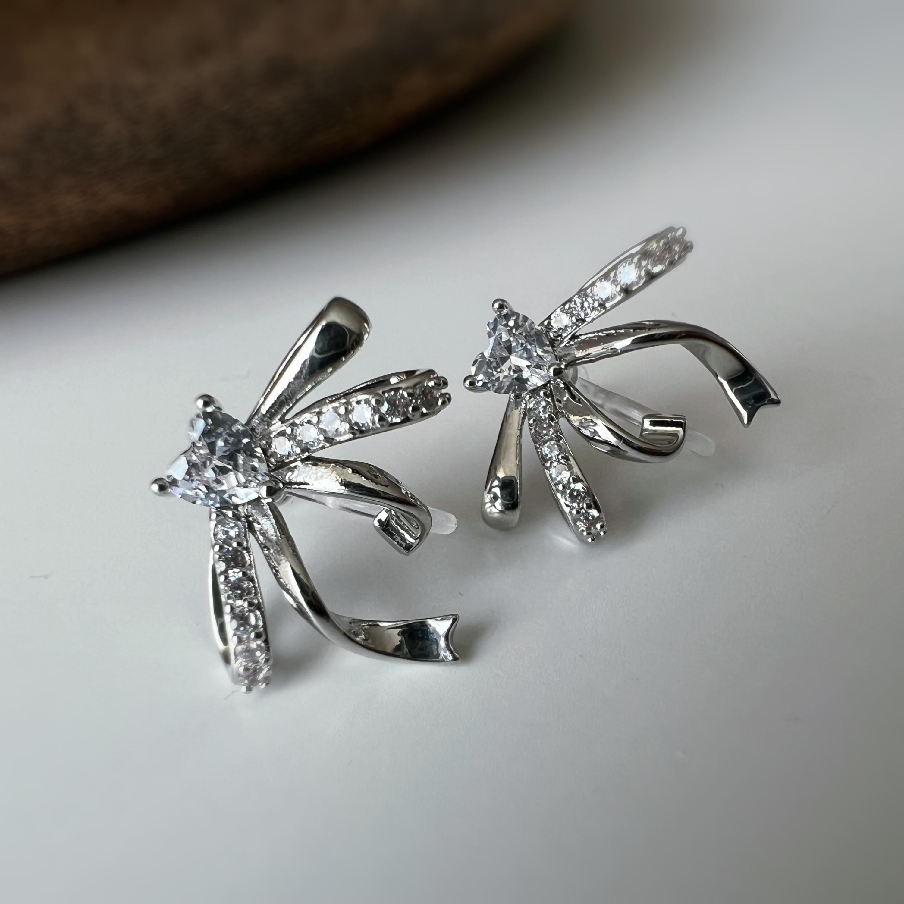 Clips d’oreilles élégants en forme de nœud scintillant Or / Argent sertis de strass étincelants. Bijou raffiné pour un style chic et féminin