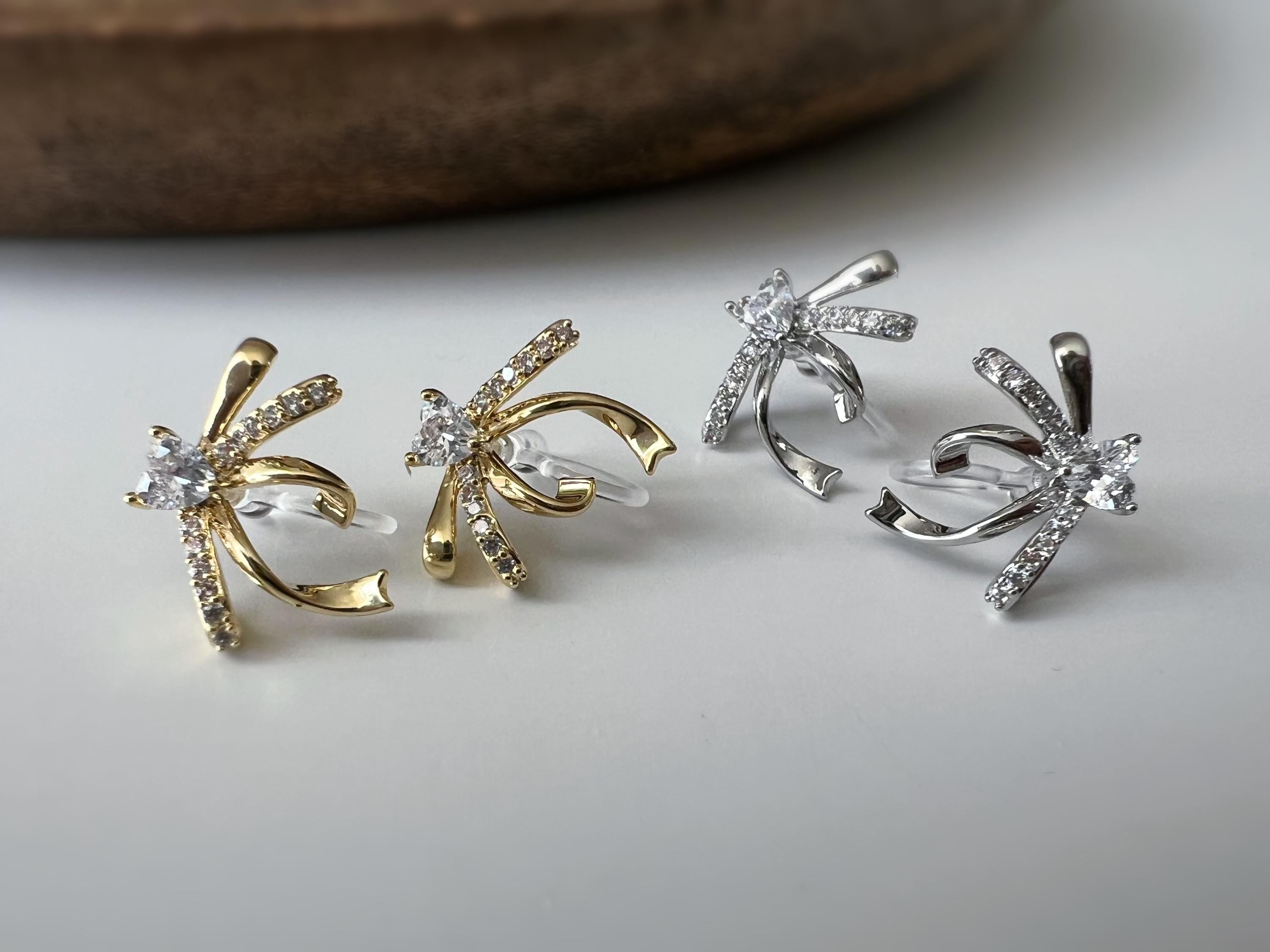 Clips d’oreilles élégants en forme de nœud scintillant Or / Argent sertis de strass étincelants. Bijou raffiné pour un style chic et féminin