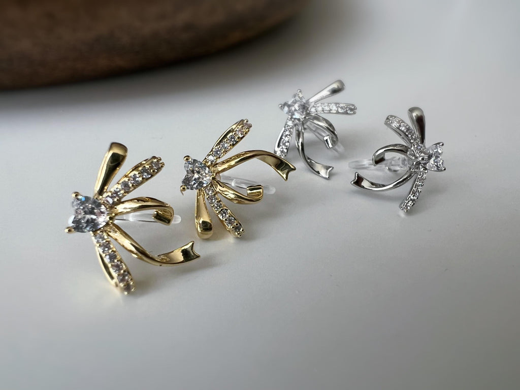 Clips d’oreilles élégants en forme de nœud scintillant Or / Argent sertis de strass étincelants. Bijou raffiné pour un style chic et féminin