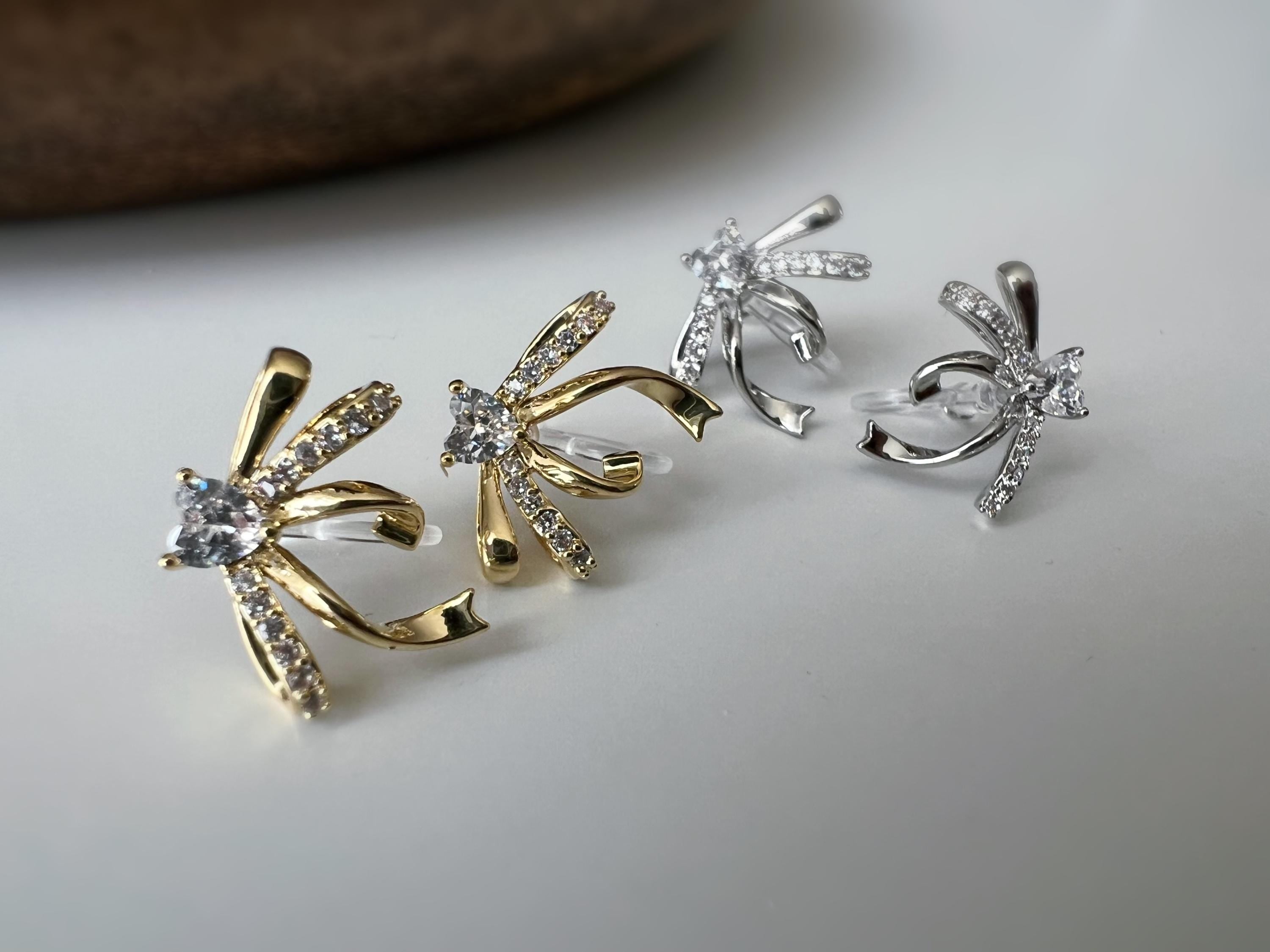 Clips d’oreilles élégants en forme de nœud scintillant Or / Argent sertis de strass étincelants. Bijou raffiné pour un style chic et féminin