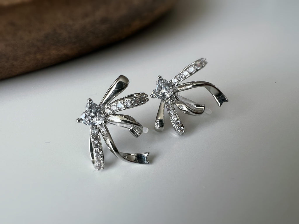 Clips d’oreilles élégants en forme de nœud scintillant Or / Argent sertis de strass étincelants. Bijou raffiné pour un style chic et féminin