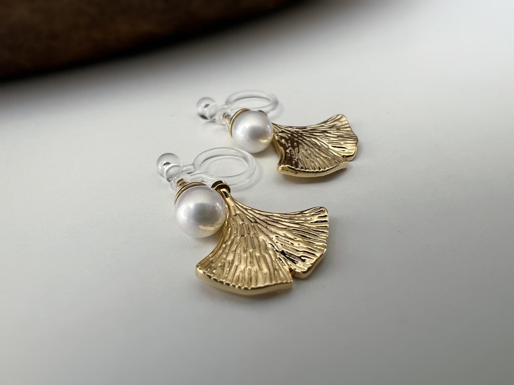 Clips d’oreilles élégants ornés d’une perle blanche et d’un pendentif feuille de ginkgo Or / Argent. Un bijou raffiné, chic et intemporel.