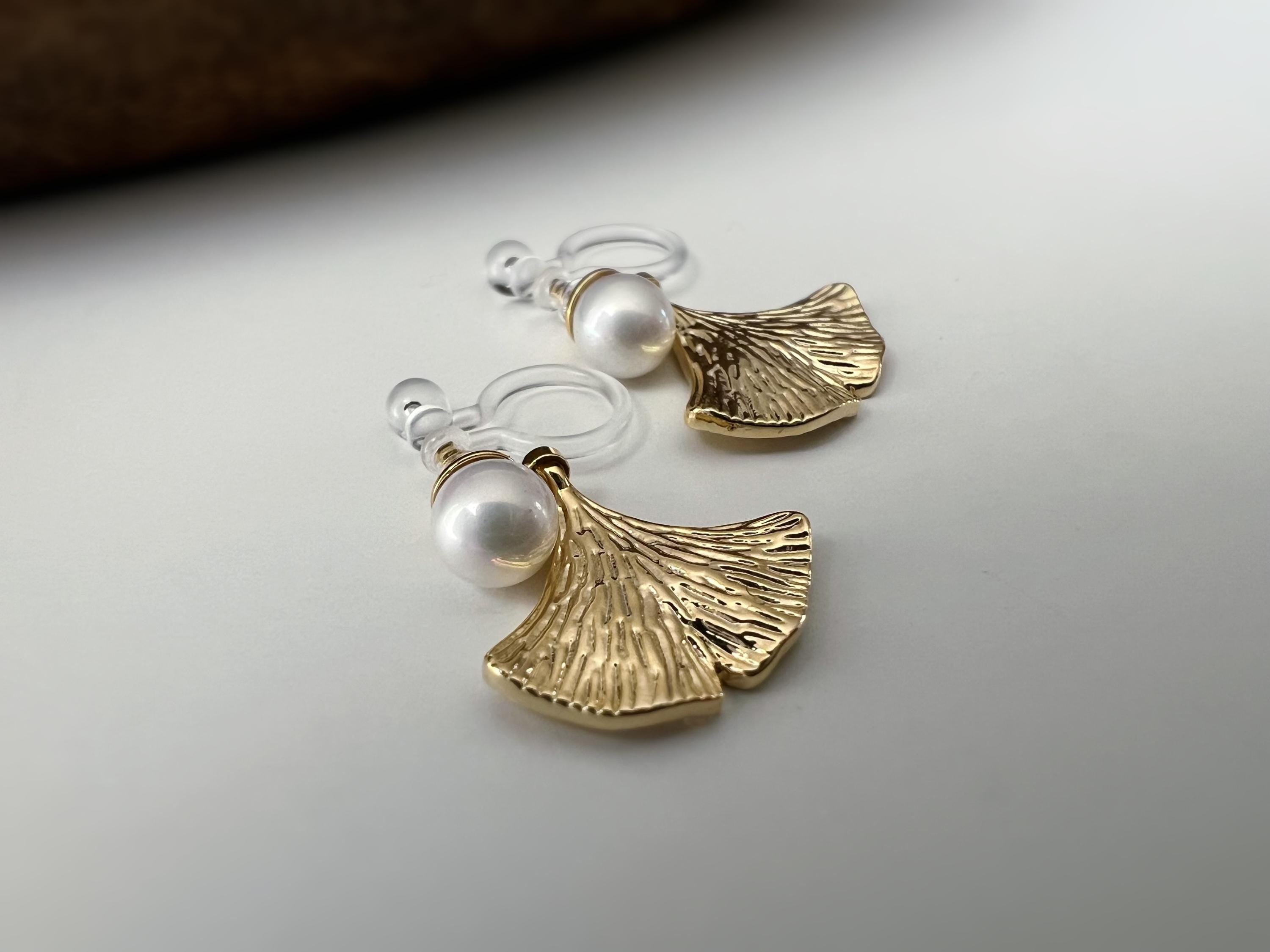 Clips d’oreilles élégants ornés d’une perle blanche et d’un pendentif feuille de ginkgo Or / Argent. Un bijou raffiné, chic et intemporel.