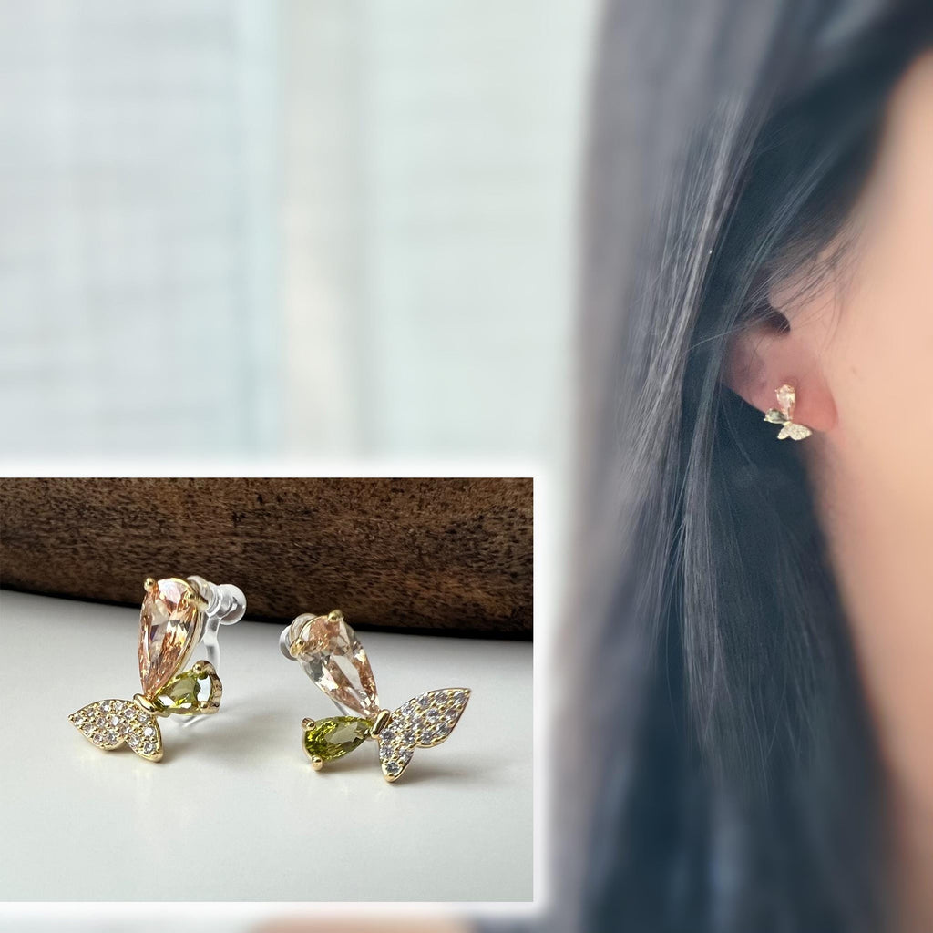 Clips d’oreilles papillon raffinés sertis de cristaux étincelants aux teintes champagne et vert olive. Un bijou délicat et lumineux.