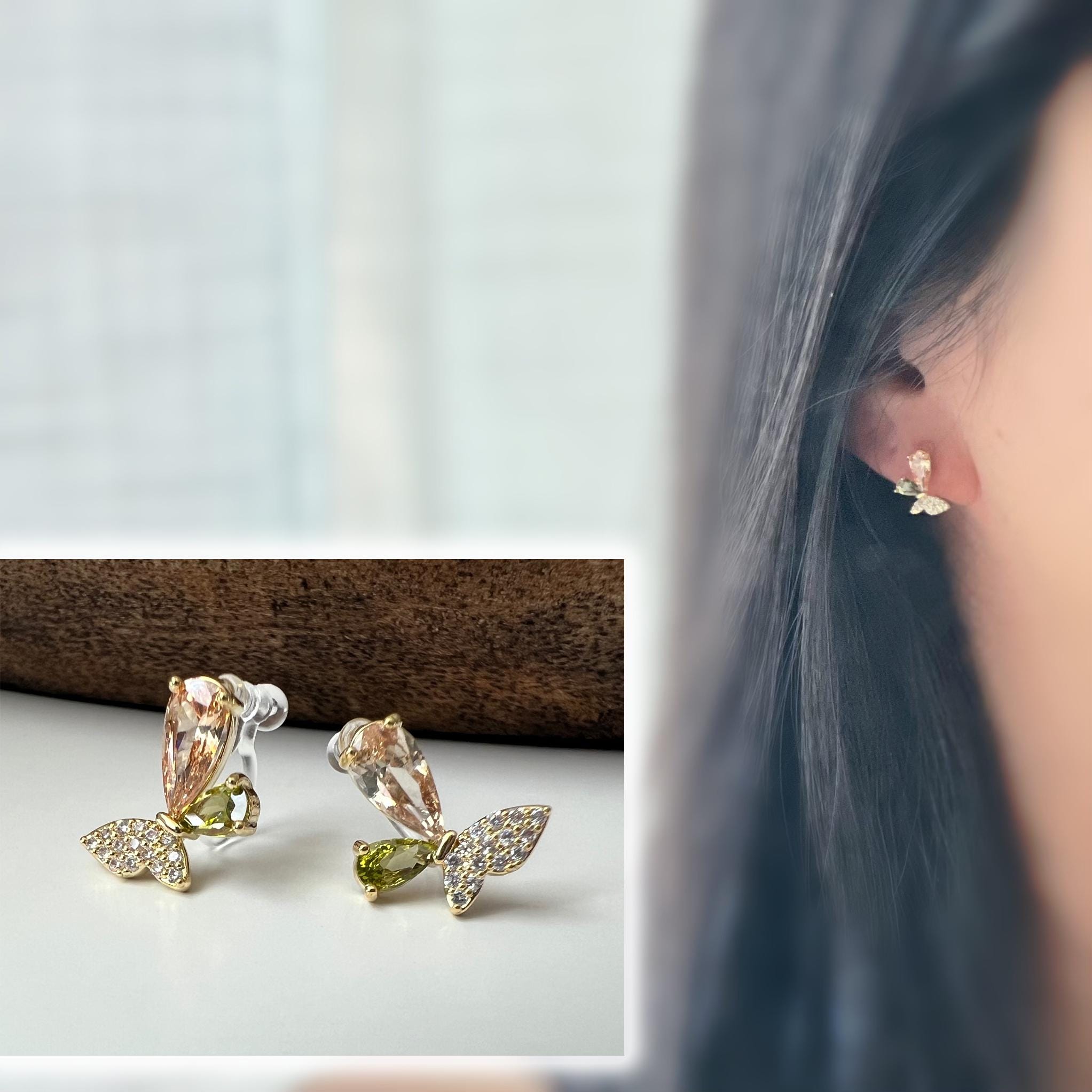 Clips d’oreilles papillon raffinés sertis de cristaux étincelants aux teintes champagne et vert olive. Un bijou délicat et lumineux.