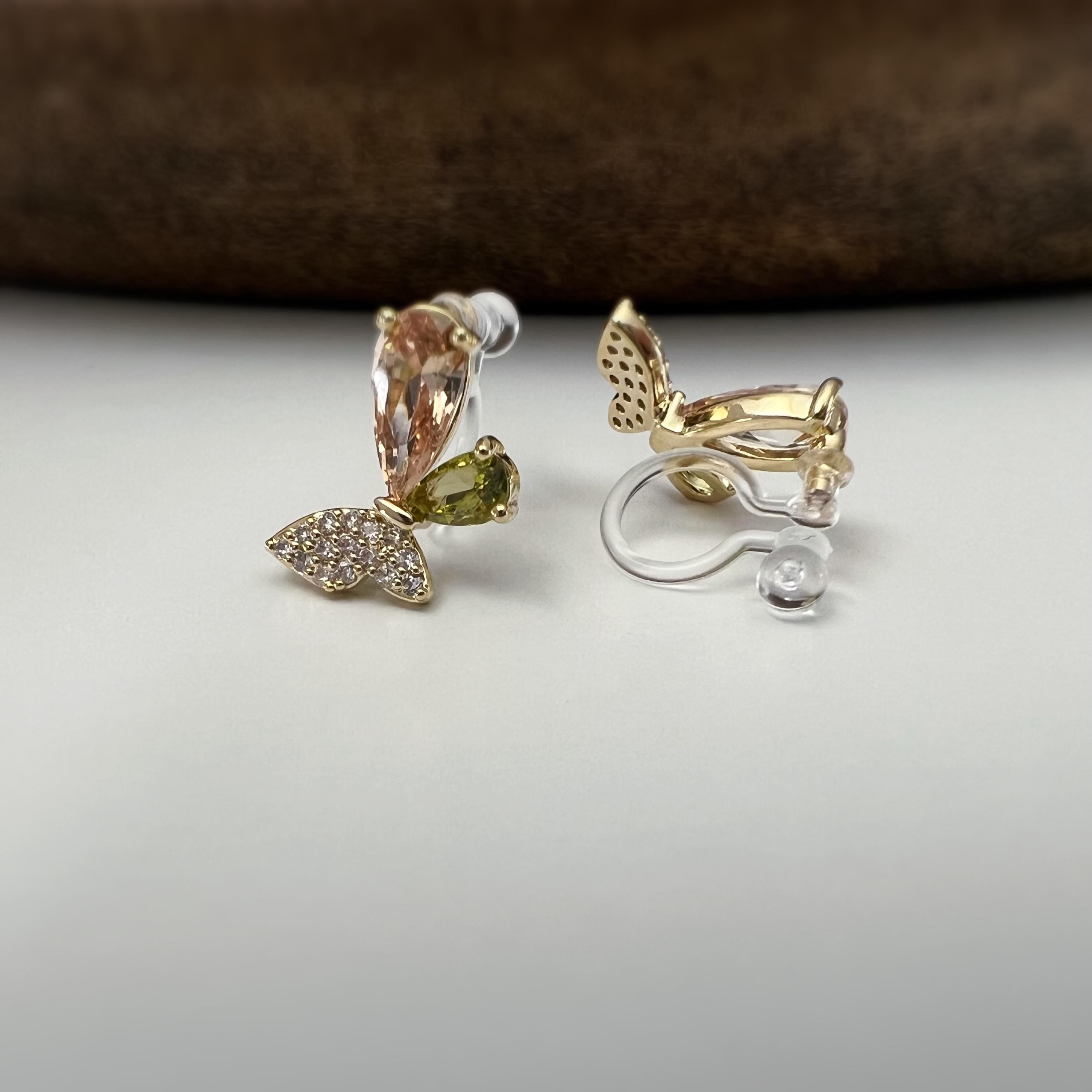 Clips d’oreilles papillon raffinés sertis de cristaux étincelants aux teintes champagne et vert olive. Un bijou délicat et lumineux.