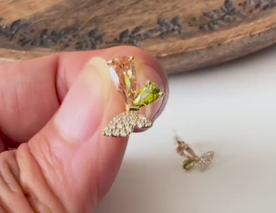 Clips d’oreilles papillon raffinés sertis de cristaux étincelants aux teintes champagne et vert olive. Un bijou délicat et lumineux.